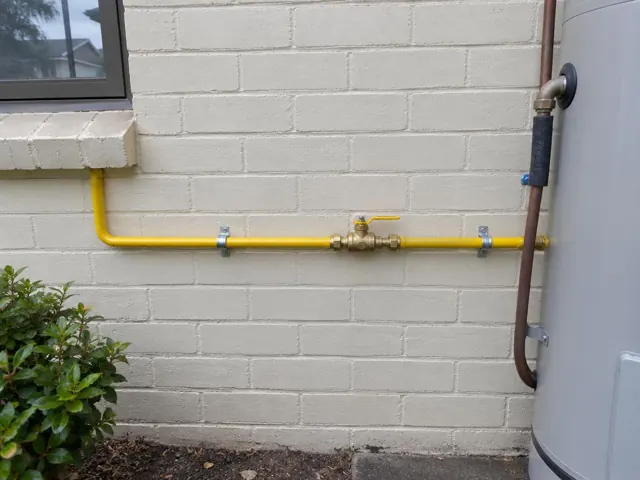 Yellow gas pipe and valve on a brick exterior wall beside a water heater in Miranda
